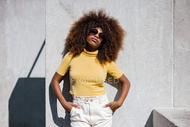 Чорна жінка з афро волоссям позує перед сірою стіною, дивлячись на камеру — стокове фото