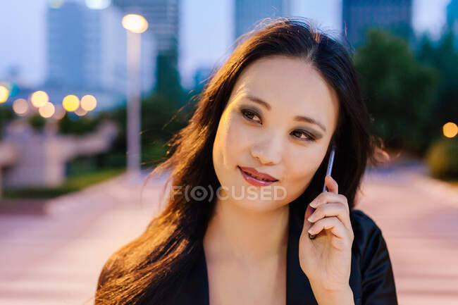 Encantado empresária asiática em pé na rua de megapolis à noite e falando no telefone móvel — Fotografia de Stock
