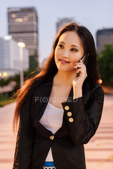 Encantado empresária asiática em pé na rua de megapolis à noite e falando no telefone móvel — Fotografia de Stock