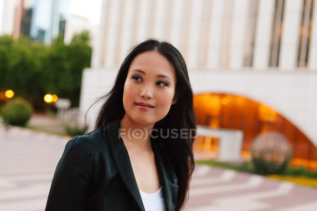 Добре одягнена етнічна жінка-підприємець, що йде по вулиці мегаполісу і дивиться в сторону — стокове фото