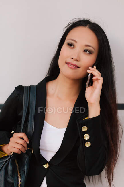 Conteúdo Empresária asiática falando no smartphone enquanto discute o projeto de negócios e olha para longe — Fotografia de Stock