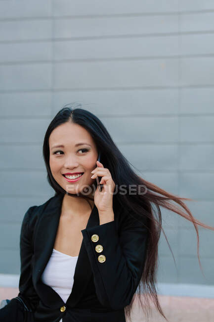 Glad ethnic businesswoman standing in street and talking on mobile phone while looking away — Stock Photo