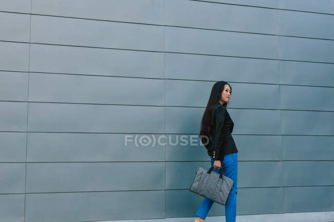 Сама впевнена в собі азіатська жінка-підприємець йде по вулиці біля міського будинку і озирається — стокове фото