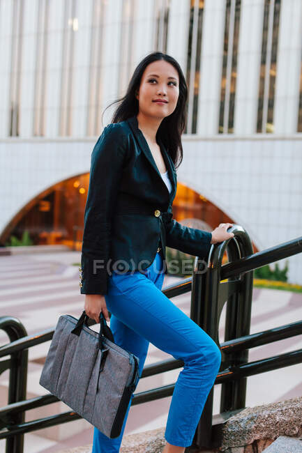 Vista lateral de empresária étnica bem vestida andando no andar de cima na rua de megapolis e olhando para longe — Fotografia de Stock