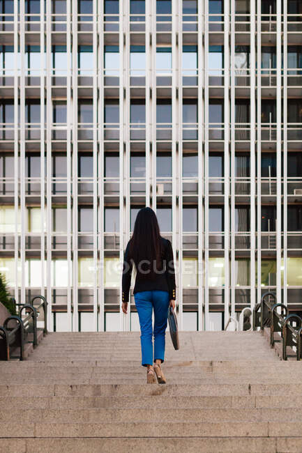 Вид ззаду на невпізнавану вдягнену жінку-підприємець, що йде нагору на вулиці Мегаполіса і дивиться геть — стокове фото