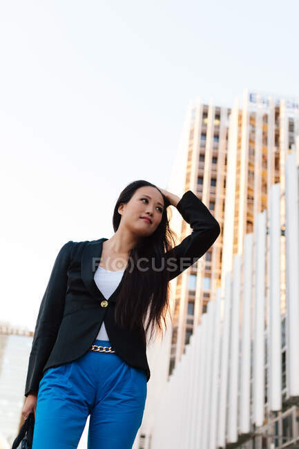 From below well dressed ethnic female entrepreneur walking on the street of megapolis and looking away — Stock Photo