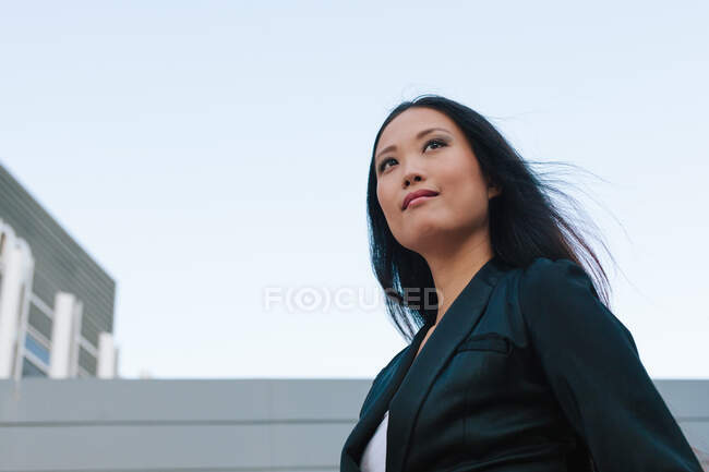 Низький кут чітко одягненої азіатської жінки-підприємця стояв з рукою в кишені на вулиці міста і озираючись — стокове фото