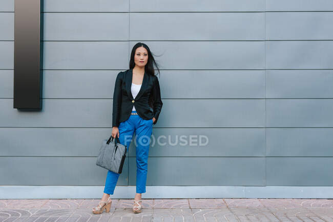 Self confident Asian female entrepreneur walking along street near urban building and looking away — Stock Photo