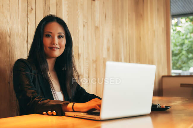 Busy Asian female entrepreneur sitting at table in cafe while eating sushi and working on remote project via netbook — Stock Photo