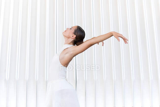 Side view of young female ballet dancer in pointe shoes with raised leg and arm dancing on tiled pavement outdoors — Stock Photo