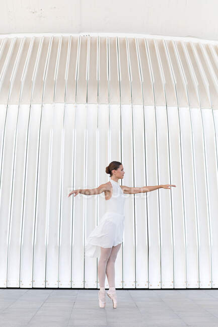 Молодая балетная танцовщица на цыпочках в пуантах с поднятыми ногами и руками танцует на тротуаре на открытом воздухе — стоковое фото