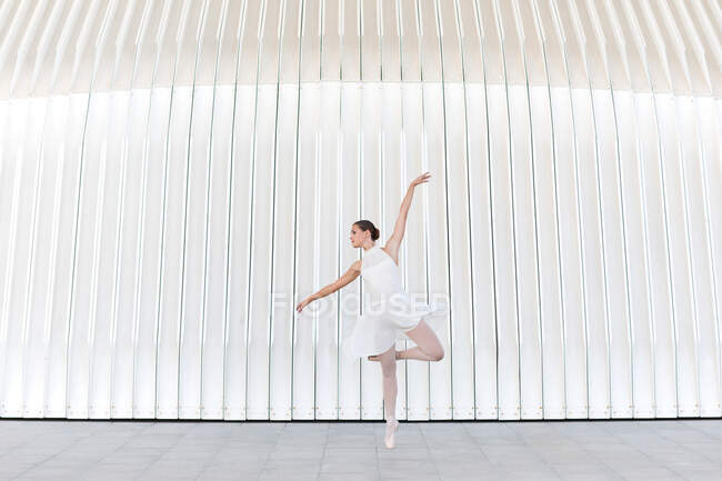 Bailarina de ballet joven en puntillas con pierna levantada y brazo bailando sobre pavimento de baldosas al aire libre - foto de stock