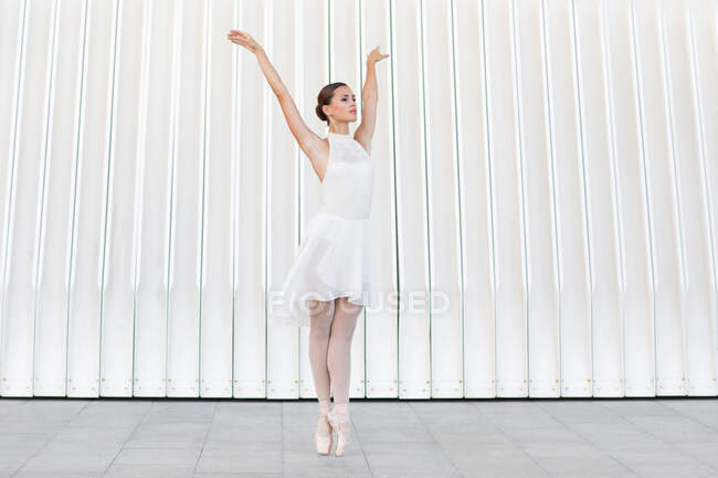 Jovem dançarina de balé feminina na ponta dos pés em sapatos pontiagudos com perna levantada e braço dançando no pavimento de azulejos ao ar livre — Fotografia de Stock