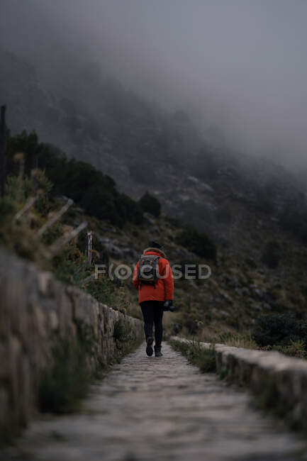 Back view anonymous backpacker in warm clothes hiking on narrow pathway in highlands covered with dense fog in Cadiz Spain — Stock Photo