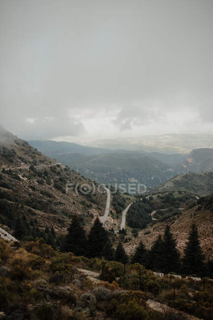 Picturesque spacious hilly terrain with greenery and trees located beneath cloudy misty sky — Stock Photo