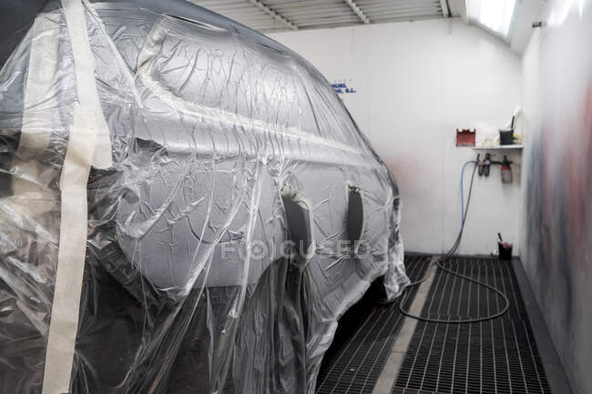 Сучасний автомобіль, покритий пластиковим матеріалом, підготовлений для фарбування і припаркований в центрі обслуговування ремонту автомобілів — стокове фото