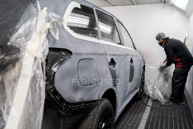 Vista laterale del lavoratore maschio che rimuove la pellicola plastica dall'auto prima di dipingere nel servizio di riparazione — Foto stock