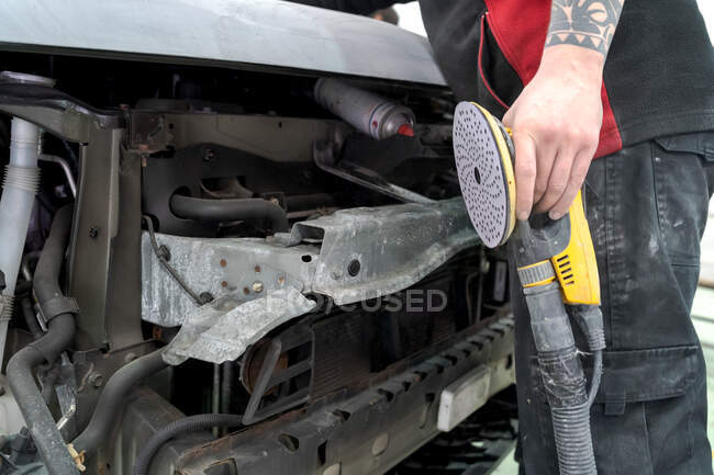 Crop meccanico maschio anonimo utilizzando la macchina per la lucidatura auto, mentre la preparazione di automobili per la pittura in officina — Foto stock
