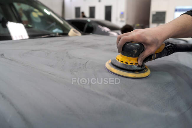 Анонимный мужчина-механик, использующий машину для полировки автомобиля при подготовке автомобиля к покраске в мастерской — стоковое фото
