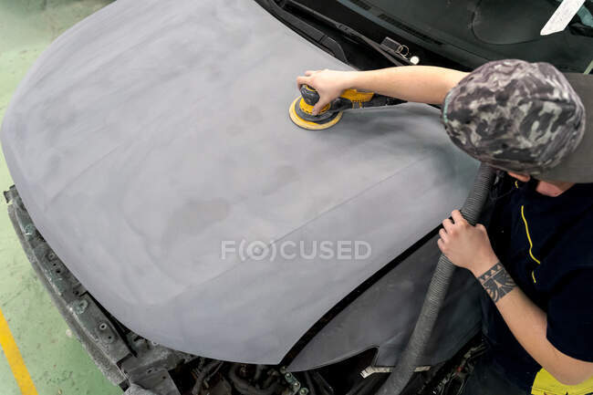 Crop anonymous male mechanic using machine for polishing car while preparing automobile for painting in workshop — Stock Photo