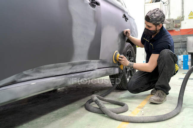 Боковий вигляд чоловічий механізм з використанням машини для полірування автомобіля під час підготовки автомобіля до малювання в майстерні — стокове фото