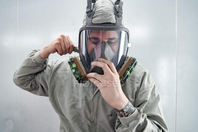 Male mechanic putting on respirator and protective suit while preparing for painting car in workshop — Stock Photo