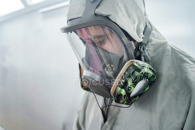 Мужчина-механик надевает респиратор и защитный костюм во время подготовки к покраске автомобиля в мастерской — стоковое фото