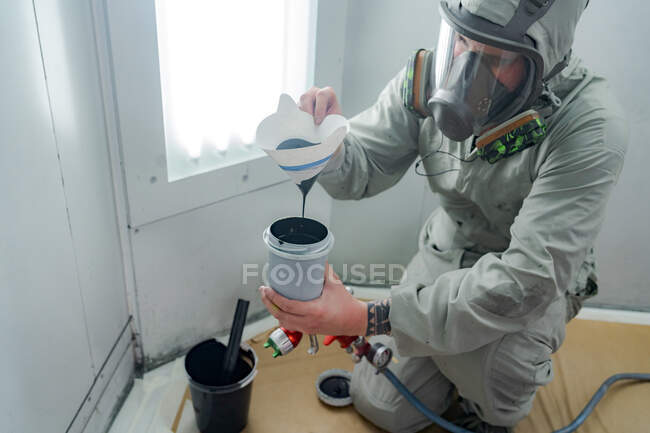 From above of male mechanic in respirator and suit filling plastic gun with paint in car service — Stock Photo