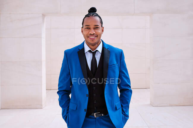Приємний афроамериканський підприємець у модному синьому костюмі стоїть з руками в кишенях у місті і дивиться на камеру. — стокове фото