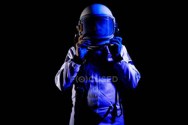 Male cosmonaut wearing white space suit and helmet while standing on black background in blue neon light — Photo de stock