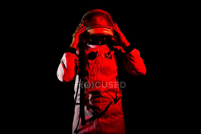 Male cosmonaut wearing white space suit and helmet while standing on black background in red neon light — Stock Photo