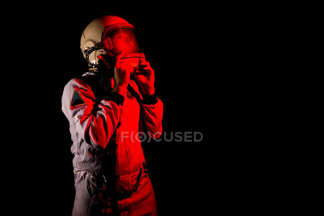 Male cosmonaut wearing white space suit and helmet while standing on black background in red neon light — Photo de stock