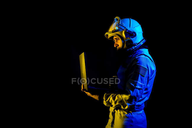 Side view of concentrated astronaut in spacesuit and helmet browsing modern netbook while standing on black background — Stock Photo