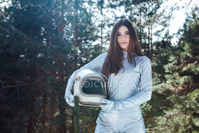 Female cosmonaut in spacesuit holding helmet in hands and standing in snowy woodland while looking at camera — Stock Photo