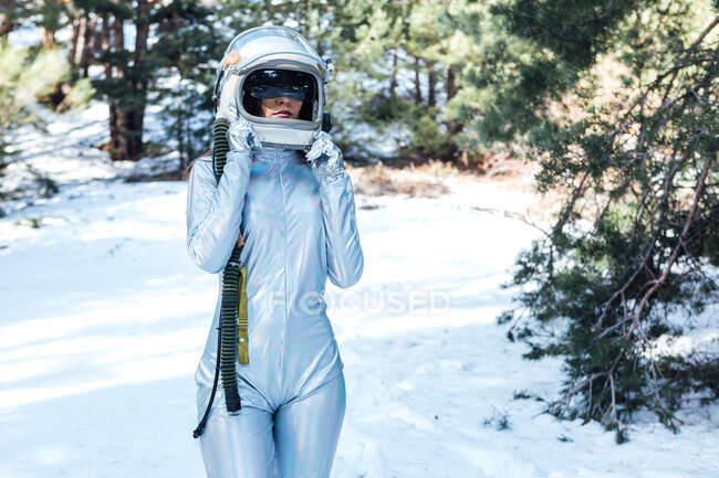 Focused unrecognizable young female astronaut in spacesuit and helmet standing in snowy woodland — Fotografia de Stock