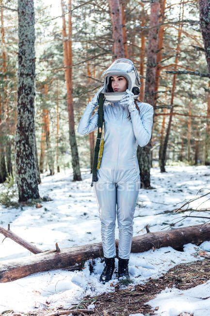 Konzentrierte junge Astronautin in Raumanzug und Helm schaut weg und steht im verschneiten Wald — Stockfoto