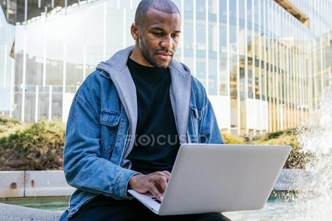 Ethnic African american adult male remote employee with laptop sitting in city — Photo de stock