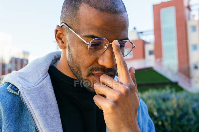 Мужской пол афро-американец трогает очки, глядя на городские здания днем — стоковое фото