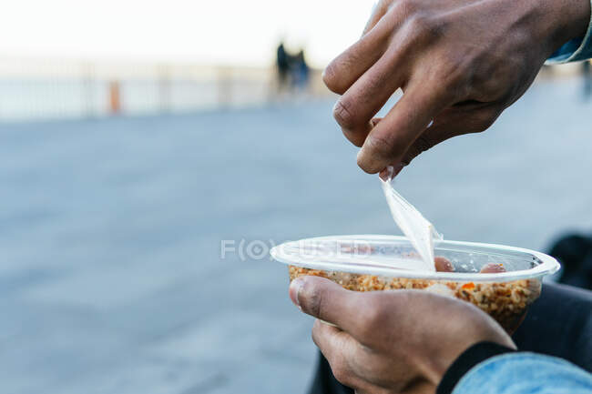 Crop anonymous ethnic male with appetizing healthy food with soft cheese cubes in plastic container to go — Stock Photo