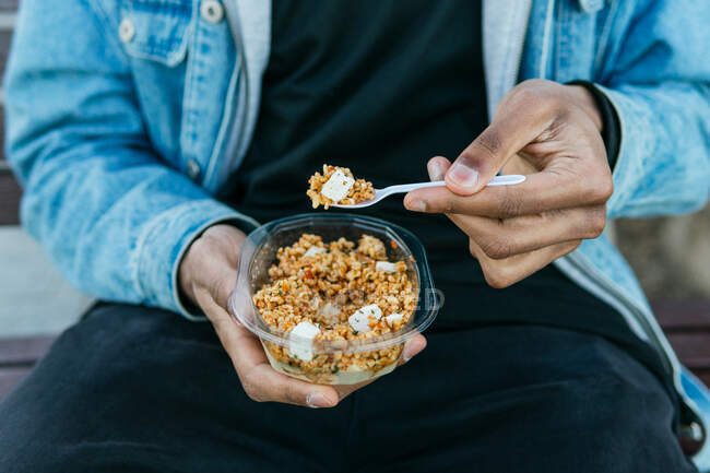 Crop anonymous ethnic male with appetizing healthy food with soft cheese cubes in plastic container to go — Photo de stock