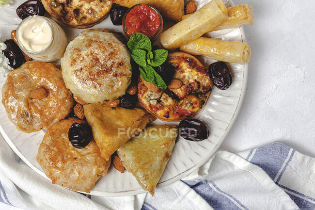 Высокий угол ассортимента вкусной арабской кухни с сальсой и свежими листьями мяты возле миндаля во время праздников Рамадан — стоковое фото