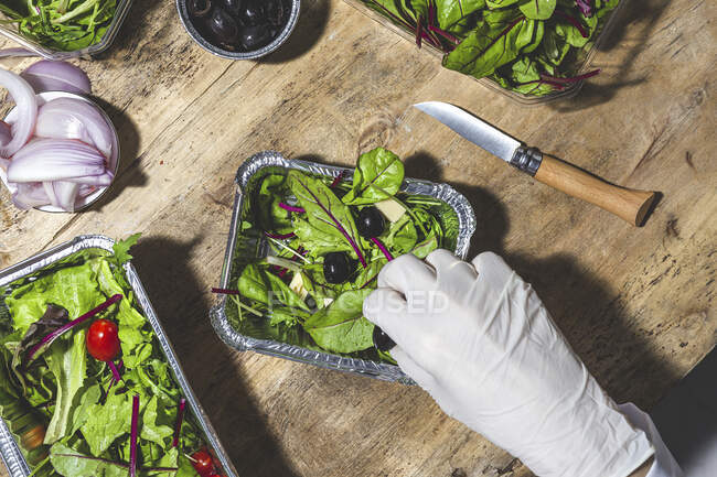 Anonymer Koch im Handschuh, der schwarze Oliven hinzufügt, um Blattsalat mit Butterwürfeln zu mischen — Stockfoto
