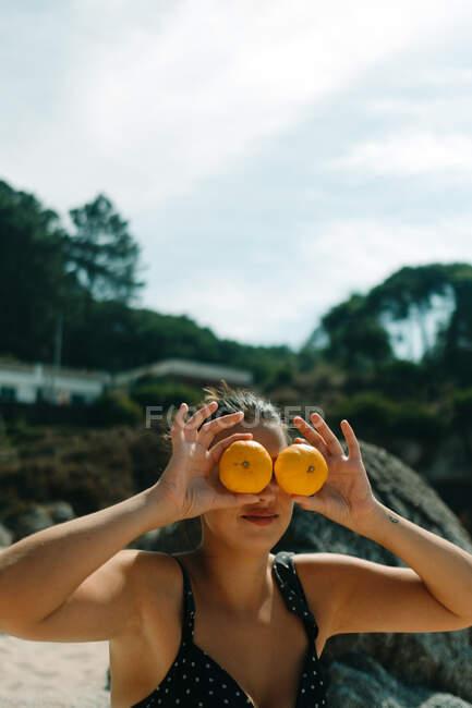 Femme sur la plage avec un bikini couvrant ses yeux avec des oranges — Photo de stock