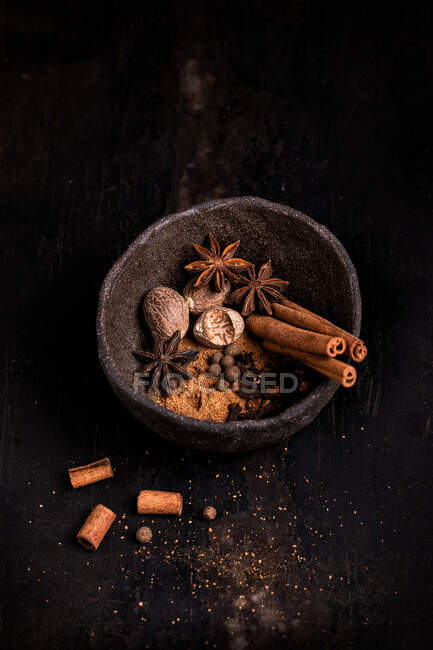 From above of wooden bowl with aromatic cinnamon sticks and anise stars with nutmeg and cloves placed on dark table — Stock Photo