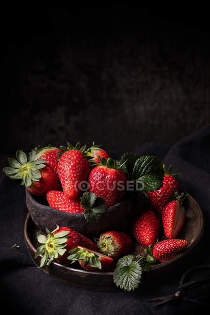 Appetitlich frische reife saftige Erdbeeren mit grünen Blättern, serviert in einer Schüssel auf dunklem Holztisch mit schwarzem Hintergrund — Stockfoto