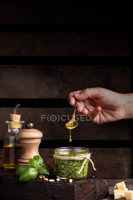 Обрізати анонімну людину з ложкою додаючи оливкову олію в горщик зі свіжоприготованим соусом песто — стокове фото
