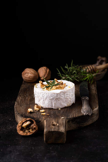 Delicioso queijo camembert gourmet decorado com nozes e alecrim fresco servido em tábua de madeira rústica — Fotografia de Stock