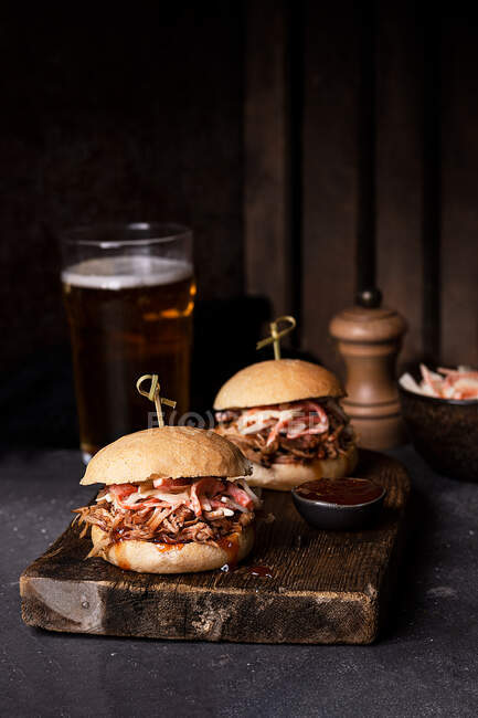 Deliciosos hambúrgueres com salada de porco e salada de salada em pães crocantes servidos em tábua de madeira rústica — Fotografia de Stock