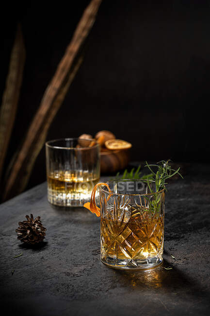 Copo de cristal de bebida de uísque à moda antiga decorado com alecrim fresco e casca de laranja na mesa preta — Fotografia de Stock