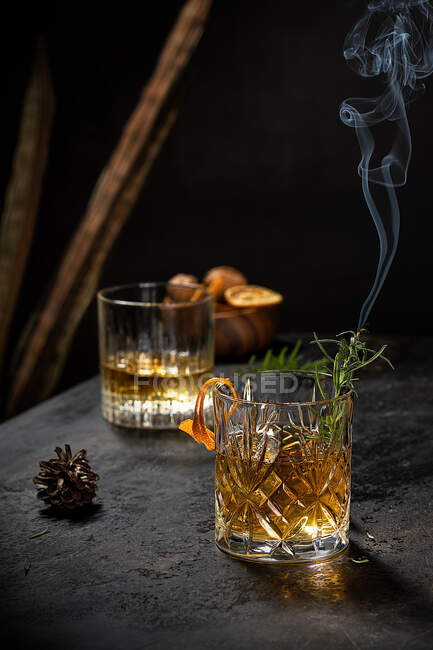 Crystal glass of old fashioned whiskey drink garnished with fresh rosemary and orange peel on black table — Stock Photo